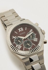 Relógio de aço inoxidável prateado com moldura octogonal, mostrador castanho, numerais romanos e três submostradores. Pulseira em estilo bracelete com elos polidos.