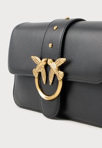 Bolsa de couro preta com aba, detalhe de fecho em forma de pássaro dourado, hardware circular e pinos decorativos na fecho para um toque extra de requinte.