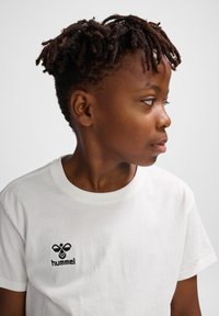 Hvid bomulds t-shirt med et lille sort "hummel" logo på venstre bryst. Rund halsudskæring, korte ærmer og glat tekstur.