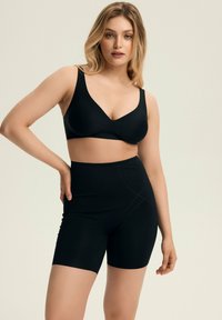 Black seamless bra with wide straps and v-neck design paired with high-waisted black shaping shorts featuring decorative stitching.