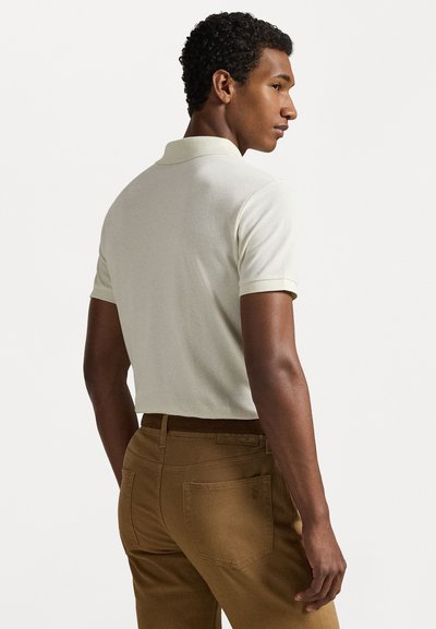 Īsās piedurknes polo krekls gaiši beigu tonī ar strukturētu audumu; saskaņots ar brūnām biksēm, kurām ir aizmugurējās kabatas un jostas birka.