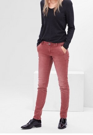 Pantalones de pana ajustados en color rosa con bolsillos laterales y cierre de botón. Combinados con una blusa negra de manga larga y zapatos negros brillantes.