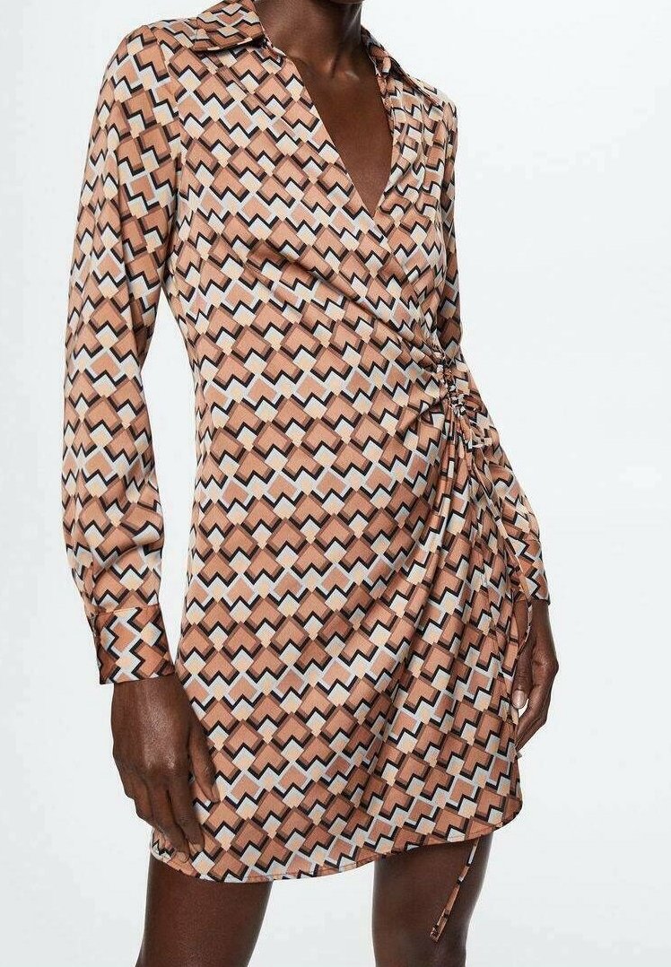 Femme portant une robe courte à manches longues avec un motif géométrique beige, noir, blanc et bleu clair, et un détail froncé sur le côté droit.