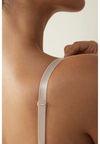 Zijdeachtige satijnen bh-band in zacht beige, met een verstelbare sluiting, tegen een gladde huid, die een verfijnd ontwerp en minimalistische stijl benadrukt.
