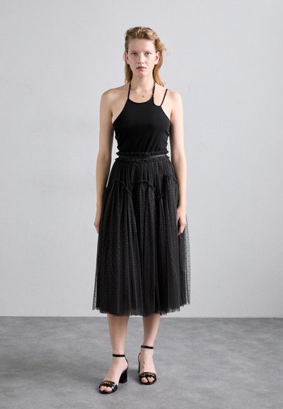 Débardeur noir à fines bretelles, associé à une jupe en tulle noire arrivant au genou avec des motifs à pois et des détails, et des sandales noires à talons.