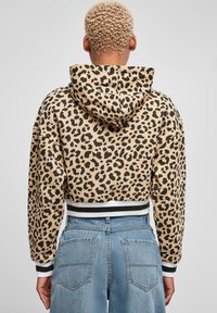 Kuttet hettejakke i beige med svart leopardmønster, med hette og stripet ribbekant og mansjetter i svart og hvitt.
