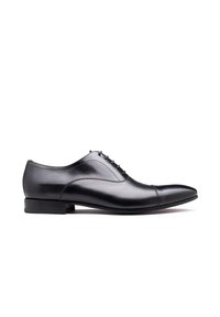 Zwarte leren oxford schoen met een gladde afwerking, puntige neus, subtiele stikdetails en een lage, gestapelde hak. Veters bovenaan.