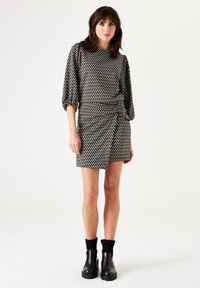 El vestido de estampado en blanco y negro cuenta con una cintura ajustada, mangas de tres cuartos y una falda fruncida. Se combina con botas negras hasta el tobillo.