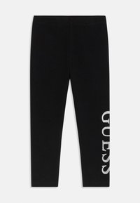 Leggings negre dintr-un material moale, având un logo „GUESS” argintiu, strălucitor, imprimat vertical pe partea stângă. Formă subțire, ajustată.