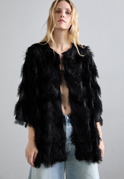 Melnā frizēta jaka ar teksturētu dizainu, atvērtu priekšpusi un platām piedurknēm. Apvienota ar gaišām džinsu biksēm.