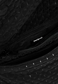 Black pouch made of textured fabric, featuring a zip closure and a "Desigual" label inside. Interior includes additional zippered compartment.