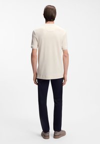 Μπεζ πόλο με κοντά μανίκια και λεπτή υφή. Διαθέτει στρογγυλό γιακά, ραφές στον ίδιο τόνο και άνετη εφαρμογή, συνδυασμένη με ναυτικό μπλε παντελόνι.