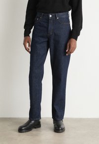 Mørkeblå denimjeans med løs passform, med frontlommer og beltehemper. Kombinert med svarte skinnankelstøvler.
