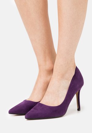 Escarpins en daim violet à talons hauts, avec une pointe effilée et un talon fin. Texture lisse et style minimaliste.
