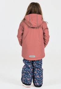 Rosa wasserdichte Jacke mit Kapuze und grauen Akzenten, kombiniert mit marineblauen Schneehosen mit Blumemuster. Sicht von hinten.