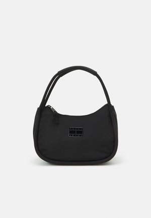 Bolso negro Tommy Jeans con doble asa, cierre de cremallera y pequeño parche con logotipo en la parte frontal, mostrado sobre fondo blanco.
