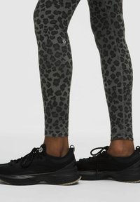 Piernas inferiores con leggings de estampado de leopardo en gris y negro, y zapatos deportivos negros sobre un fondo claro.