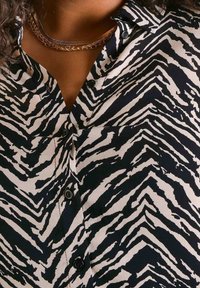 Zwart en crèmekleurig shirt met zebra-stripes en knopen langs de knooplijst, gemaakt van een zachte, gestructureerde stof. Meerdere zichtbare kraaglagen.