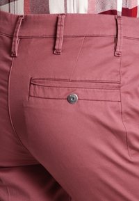 Dark pink trousers featuring a back pocket with a button closure and a smooth texture, paired with a checkered shirt.