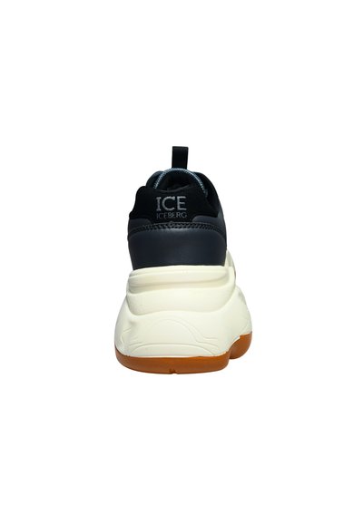 Baskets épaisses en noir et blanc avec semelle orange, affichant le logo "ICE ICEBERG" sur la languette du talon, vues de dos.