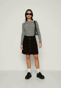 Svītrots garām piedurknēm tops, melns korduroja A-silueta svārki ar priekšējiem pogām, melni platformas apavi un maza melna rokassoma.