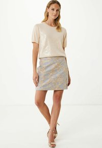Haut rose pâle à manches courtes orné de sequins, associé à une mini-jupe en dentelle florale bleu pastel et des talons à bride de cheville beiges. Design et texture simples.