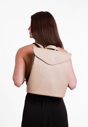 Beige leather backpack with a flap closure and textured surface. Features adjustable straps and subtle logo at the bottom.