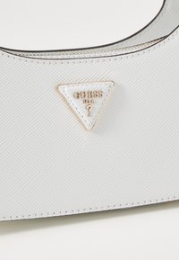 Borsa a tracolla sintetica bianca con finitura texturizzata, logo triangolare oro e bianco, e chiusura con zip con cuciture a contrasto.