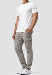 Biała koszulka z krótkim rękawem w połączeniu ze jasnoszarymi spodniami cargo z bocznymi kieszeniami i kontrastowymi szwami. Białe sneakersy dopełniają wygląd.