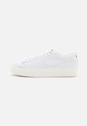 Biały niski sneaker z sznurowanym wzorem, grubą podeszwą i subtelnym logo Swoosh z boku, pokazany na gładkim jasnym tle.