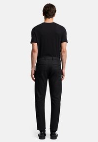 Maglietta nera a girocollo e jeans scuri su misura. Design slim-fit con due tasche posteriori e una texture liscia. Calzature: scarpe nere.