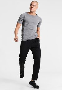 T-shirt sportif gris à manches courtes avec un tissu texturé et des accents noirs, associé à un pantalon noir ajusté et des chaussures de sport noires.