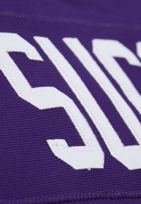 Nahaufnahme von weißen gestickten Buchstaben auf lila Stoff, die Textur und detaillierte Nähte auf der Textiloberfläche zeigen.
