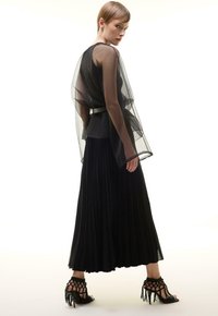 Zwarte geplooide rok gecombineerd met een doorzichtige zwarte overlay-top, cinched op de taille met een riem, aangevuld met gestructureerde hoge hakken.