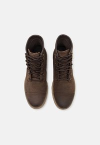 Zapatos de caña alta marrones, hechos de ante y cuero, con punta redonda, cordones en la parte delantera y suela de goma. Diseño texturizado con acentos de color contrastante.