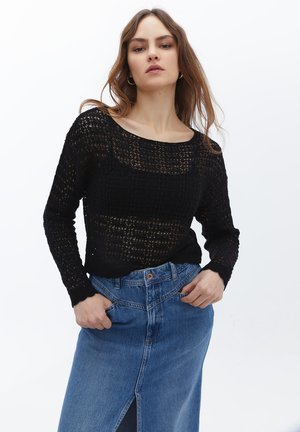 Zwarte open-gehaakte trui met lange mouwen, wijd decolleté en een textuurpatroon, gecombineerd met een lichtblauwe denimrok met een split aan de voorkant.