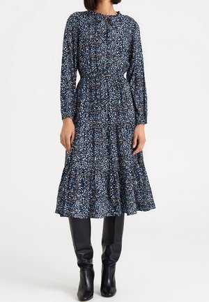Woman wearing a long-sleeve navy blue midi dress with small floral print, paired with black knee-high leather boots.