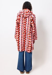 Colorful patterned coat featuring a hood, with geometric shapes in red, pink, and various colors. Paired with wide-leg blue jeans.