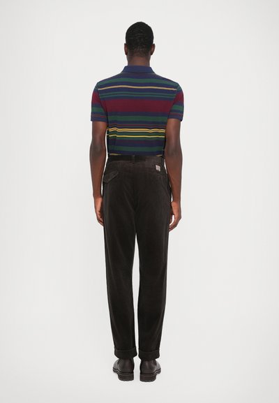 Polo cu dungi în albastru închis, verde și burgund, purtat cu pantaloni din catifea căptușită de culoare maro. Outfitul are o croială dreaptă și manșete răsucite.