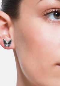 Sølv sommerfugl stud øreringer med polert metalloverflate og avrundede kanter, vist på en modells øre mot en nøytral bakgrunn.