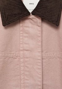 Camicetta di stoffa rosa con colletto in corduroy marrone, caratterizzata da un design dritto e cuciture visibili. Due tasche anteriori sono delineate.