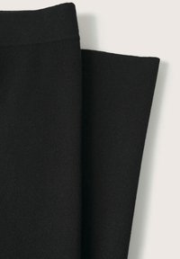 Pantalon en maille noire plié à plat, montrant la ceinture et les jambes du pantalon sur un fond clair.