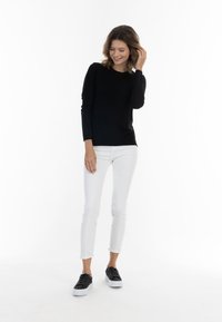 Top negru cu mânecă lungă, realizat dintr-un material neted, asociat cu blugi skinny albi și adidași negri cu talpă albă. Design simplu și casual.