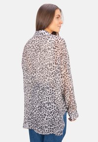 Sheer long-sleeve shirt featuring a leopard print pattern in shades of gray on a light beige background. Relaxed fit with buttoned cuffs.