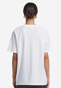 Hvid kortærmet T-shirt med rund halsudskæring, afslappet pasform, glat tekstur og en ensfarvet ryg. Ingen synlige mønstre eller detaljer.