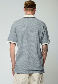 T-shirt polo à col en gris avec un motif texturé, présentant des accents crème sur les manches et le col. Manches courtes, coupe décontractée.