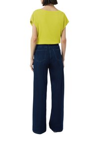 Żółta paskowa bluzka z krótkim rękawem zestawiona z ciemnoniebieskimi spodniami o szerokich nogawkach. Materiał wydaje się gładki, a spodnie mają dwie tylne kieszenie.