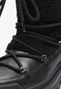 Botín negro de tobillo con un elegante upper de lana texturizada y suave, diseño de cordones negros, detalles de metal plateado y suela de goma gruesa.