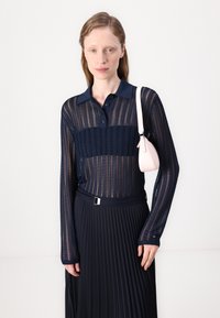 Top lung cu dantelă de culoare bleumarin, cu guler și design în straturi, acompaniat de o fustă plisată bleumarin și o geantă mică de culoare roz deschis.