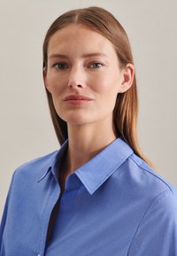 Lichtblauw overhemd met knoopsluiting en kraag, gemaakt van een gladde stof. Zichtbare stikseldetails en een comfortabele pasvorm.